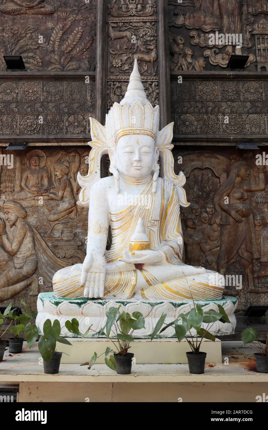Una statua buddista di Bodhisattva bianca e dorata contro un gelo di legno intricato, Tempio di Ganagaramaya, Colombo, Sri Lanka Foto Stock