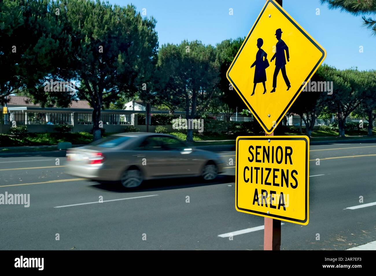 Segnale di traffico giallo che dice Senior Citizens Area con grafica di anziani che camminano . La vettura è sfocata durante la guida in background Foto Stock