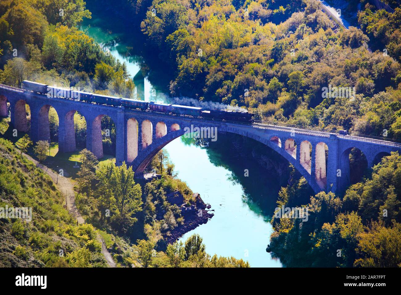 Un treno a vapore vecchio stile pieno di turisti mentre si attraversa il Ponte Solkan in una bella giornata Foto Stock