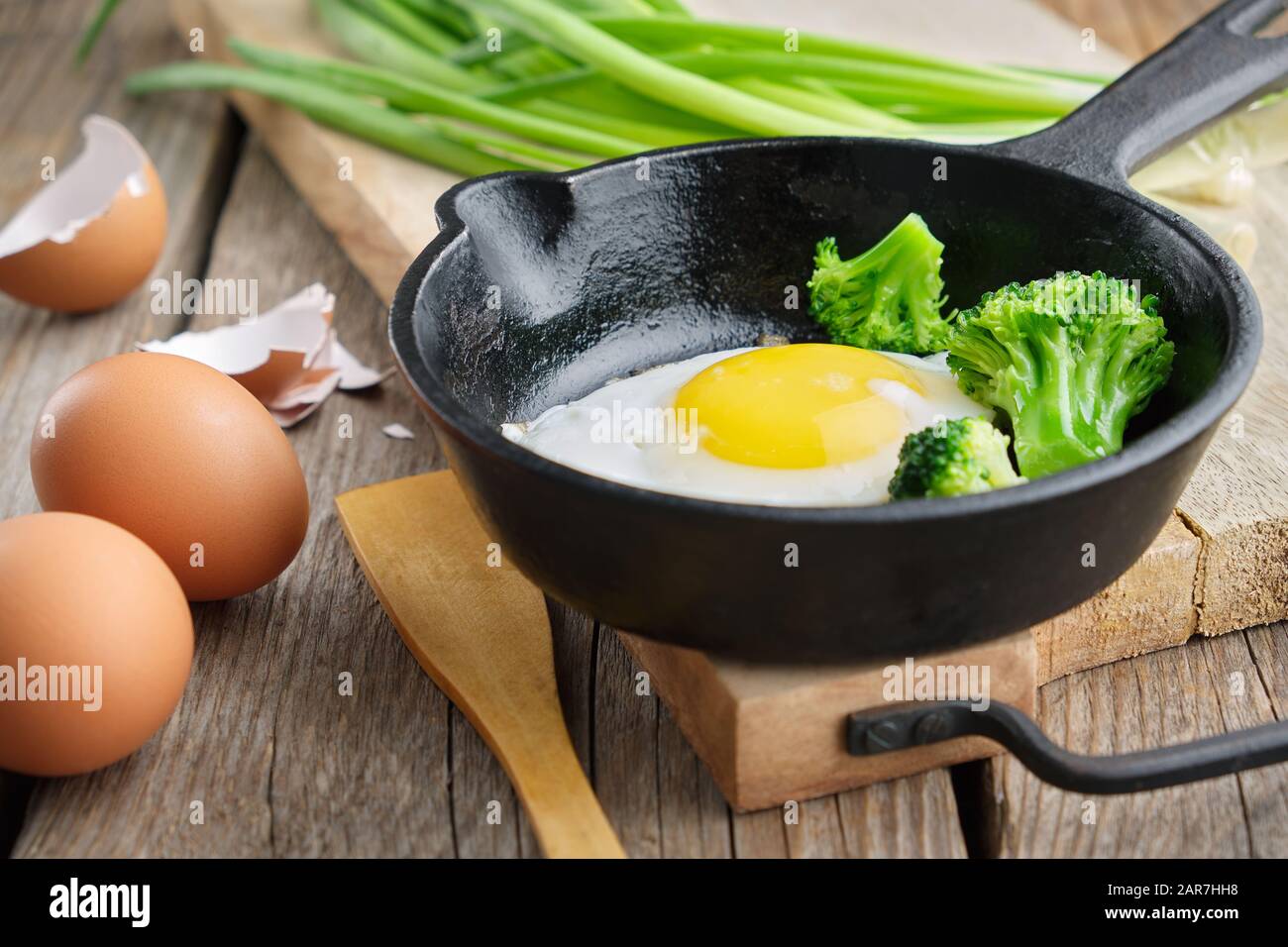 Uovo fritto con broccoli su una padella di ferro. Cipolla verde su tagliere. Foto Stock