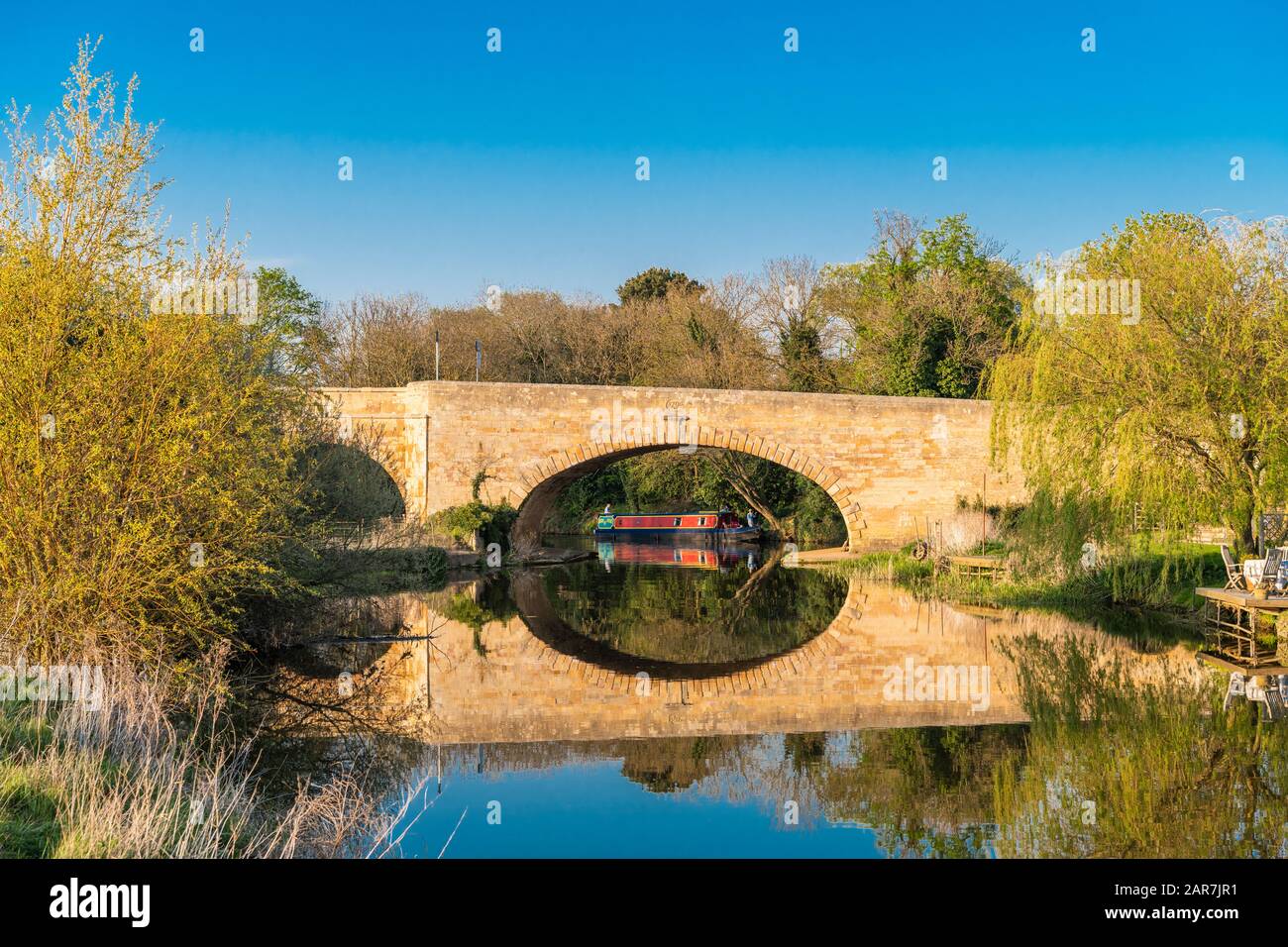 Il fiume Nene a Wansford, Cambridgeshire, Inghilterra, Regno Unito, con ponte di pietra calcarea giurassica in una tranquilla giornata di sole ad aprile e riflessioni in acqua Foto Stock