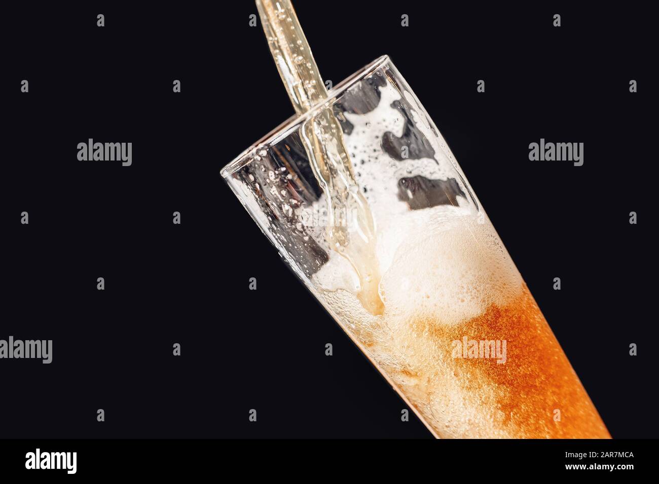 Il getto di birra fresca e leggera viene versato in un calice di vetro su sfondo scuro con spruzzi e schiuma Foto Stock