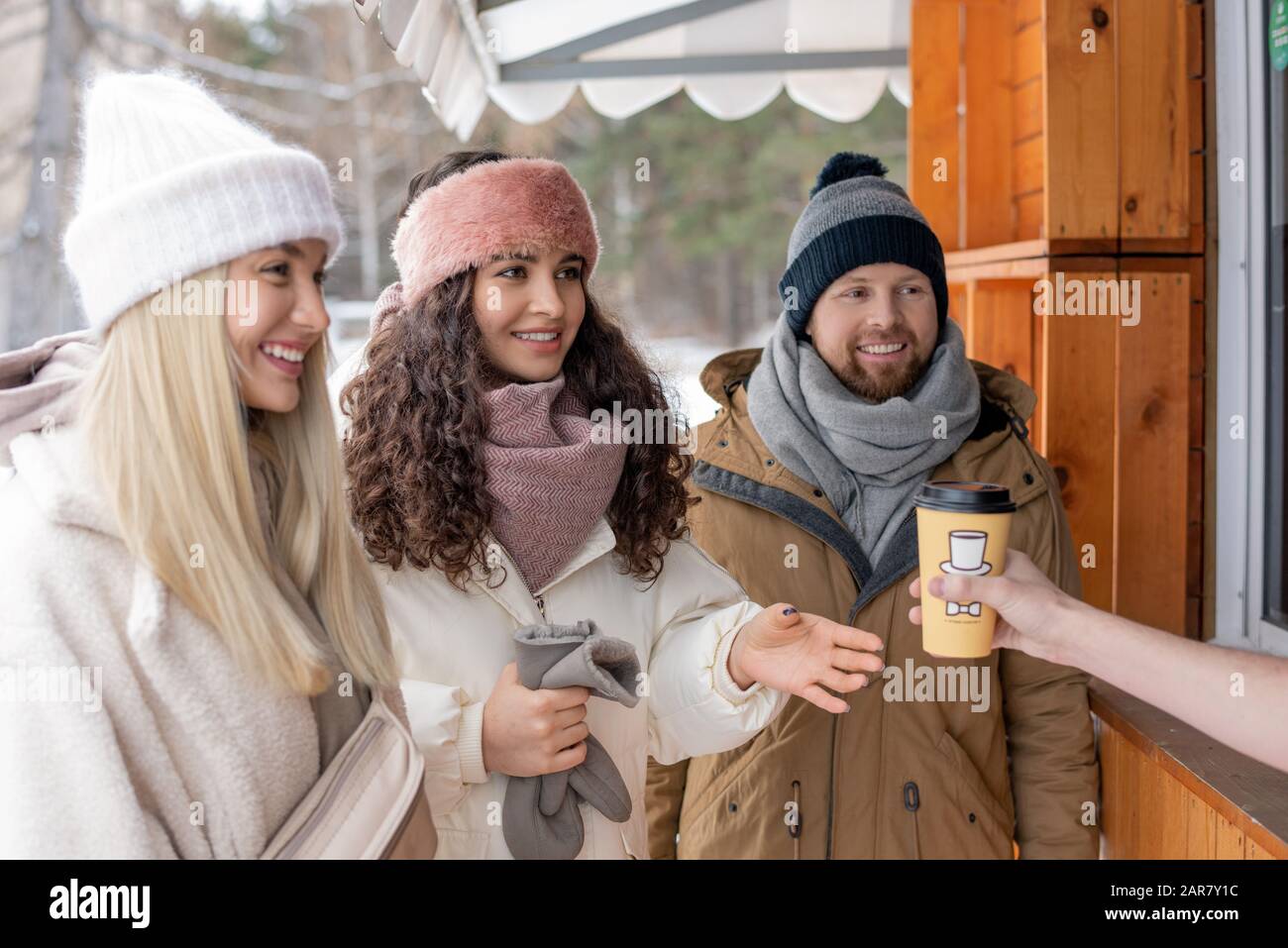 Felici giovani amici in casual winterwear acquistare caffè caldo in stalla di legno Foto Stock