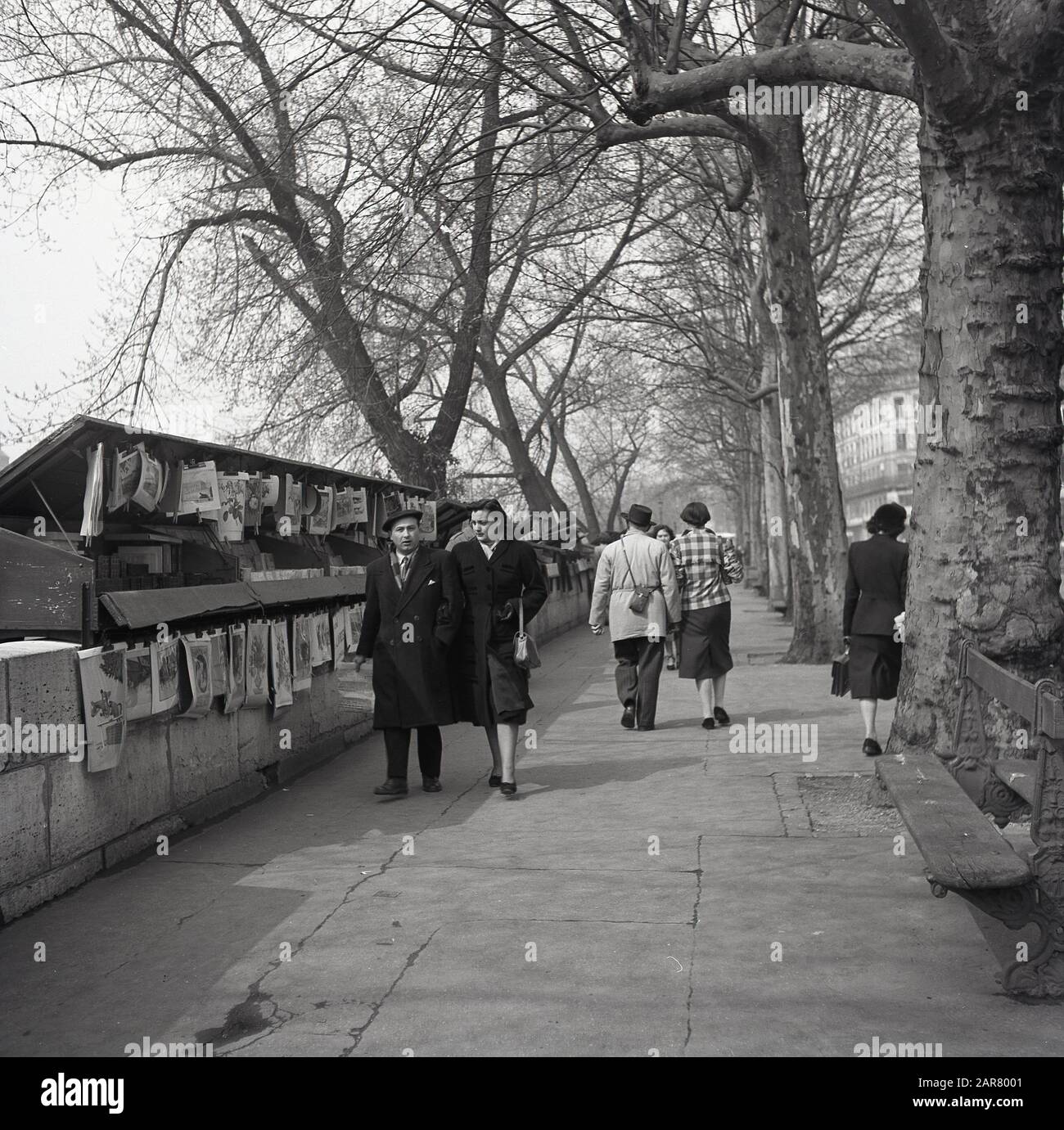 Anni '1950, coppie storiche che camminano lungo il marciapiede sulla riva della Senna, Parigi, Francia, oltrepassano le librerie conosciute come i bouquinistes di Parigi che vendono libri usati e antiquari. Foto Stock