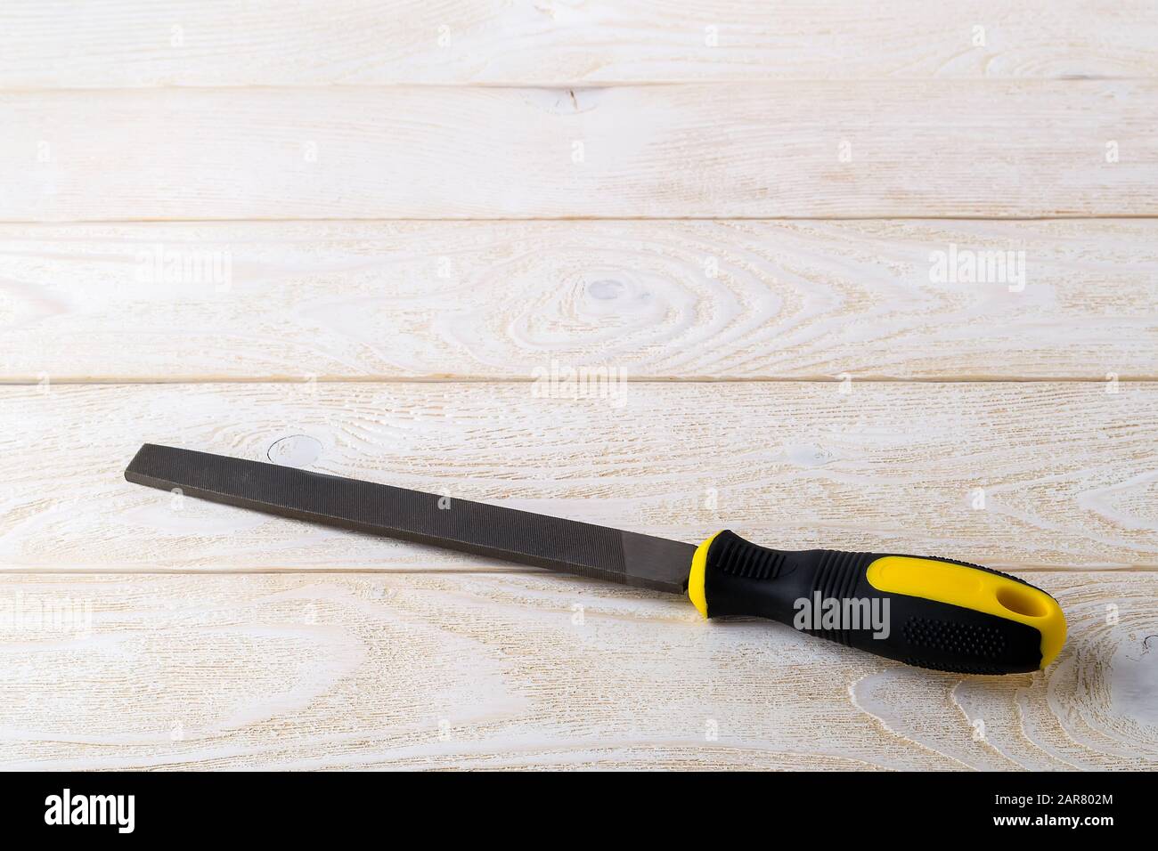 Lima piatta in acciaio con manico in gomma nera gialla su una superficie in legno bianco. Utensile rasp per la lavorazione di legno e metalli. Riparazione e costruzione. Foto Stock