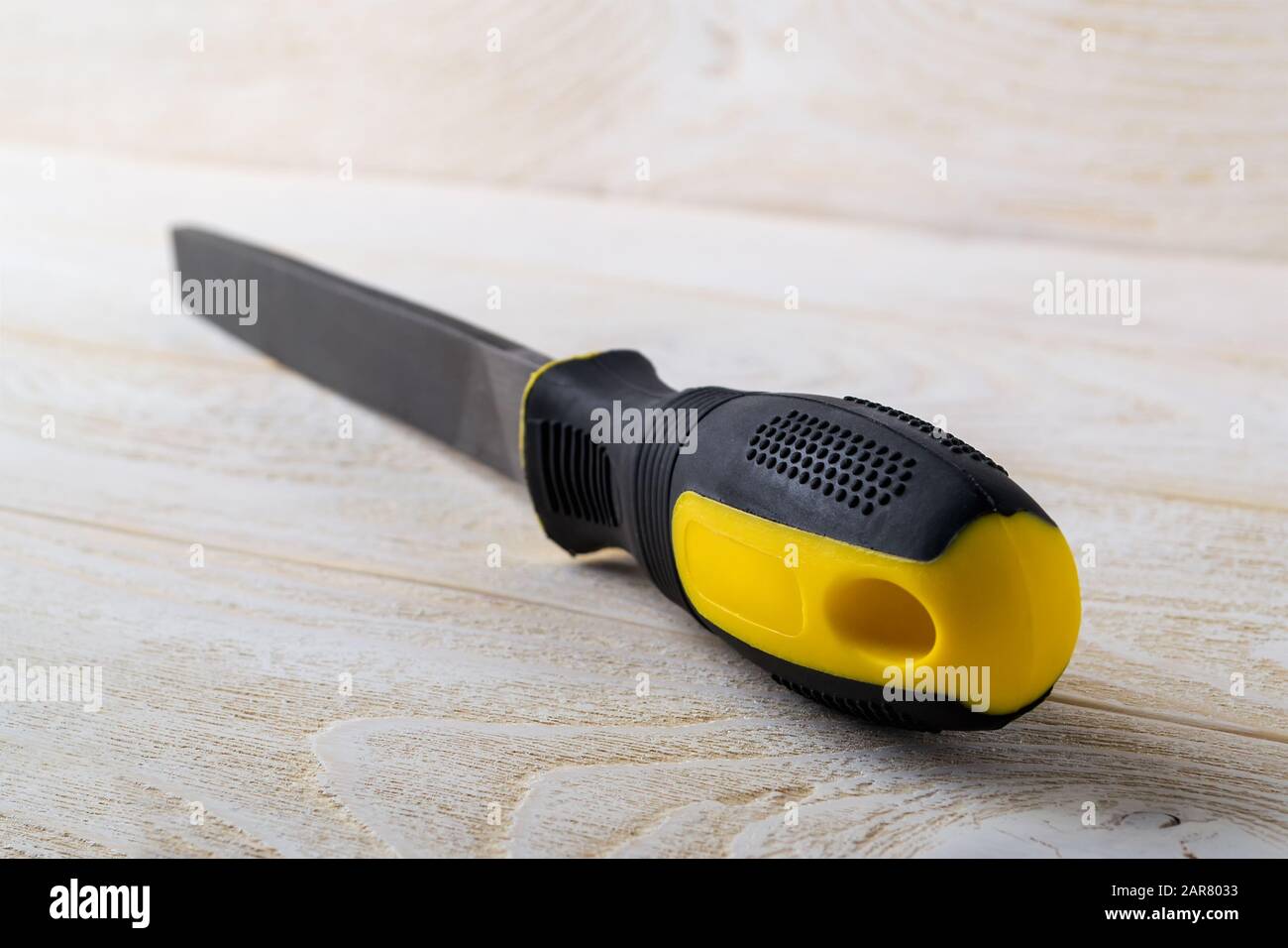 Lima piatta in acciaio con manico in gomma giallo nero su una superficie in legno bianco. Utensile rasp per la lavorazione di legno e metalli. Riparazione e costruzione. Foto Stock