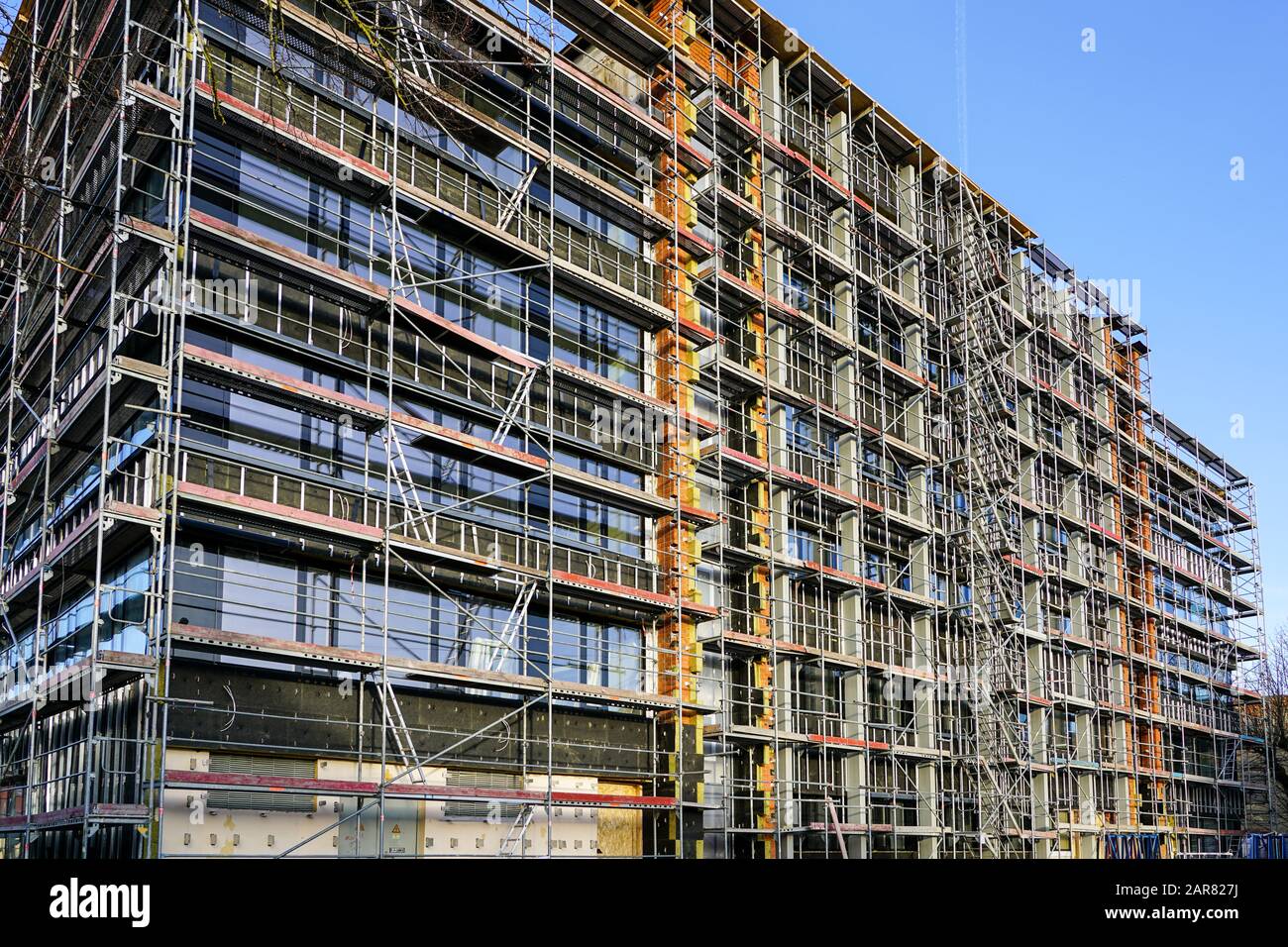 Ponteggio intorno alla casa per installare l'isolamento termico della facciata di edificio, lavoratori in giubbotti di sicurezza e caschi Foto Stock