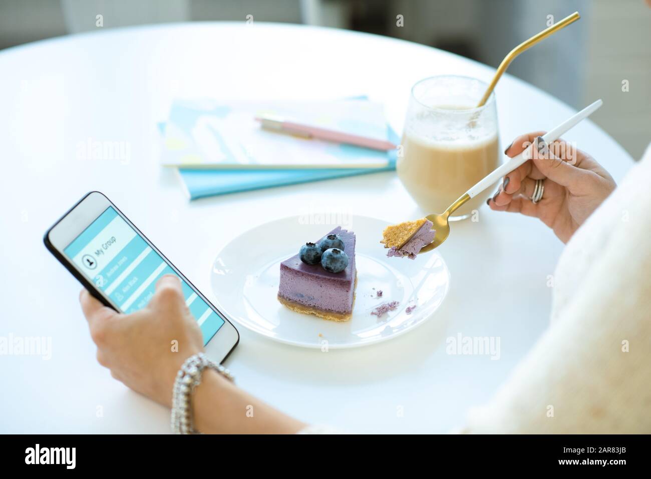 Mani di giovani donne che scorrono in smartphone e mangiare torta appetitosa Foto Stock