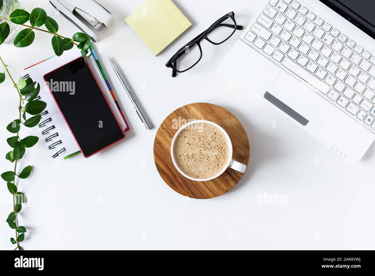 Spazio di lavoro con laptop, diario e una tazza di caffè su sfondo bianco. Elegante scrivania da ufficio in colore bianco con vaso fiorito. Disposizione piatta. Vista dall'alto. Foto Stock