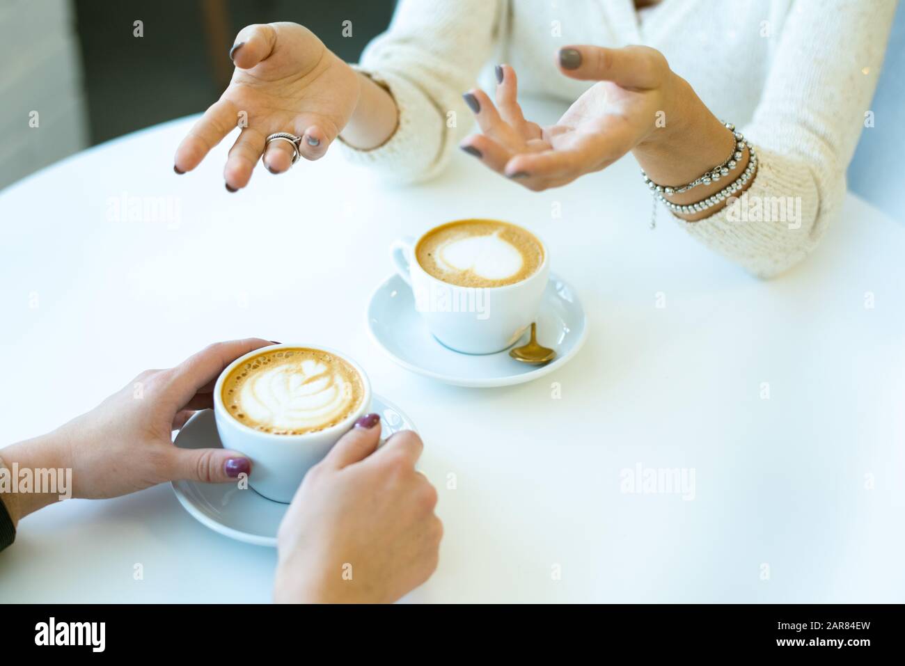 Mani di giovane femmina che parlano con la sua amica davanti da una tazza di cappuccino Foto Stock