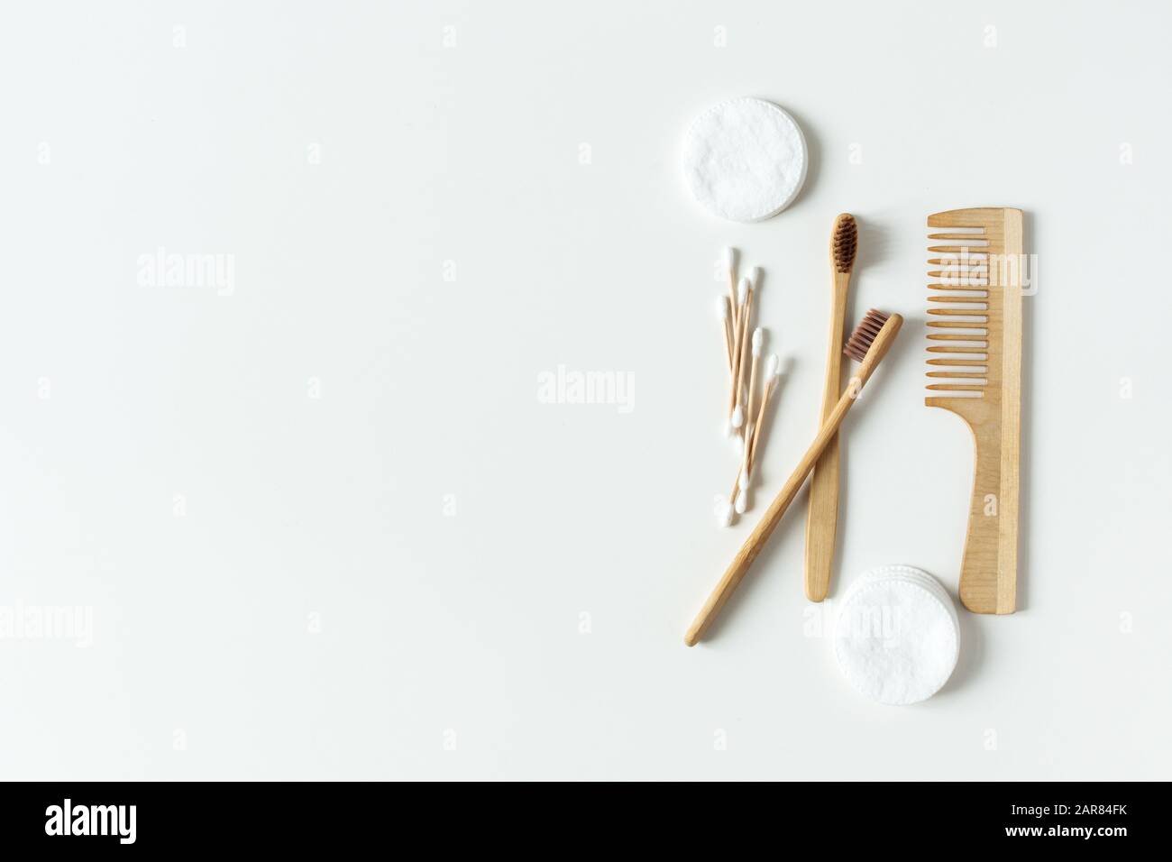 Due spazzolini da denti in bambù biodegradabile, compostabili, spazzola per capelli e tamponi in cotone su fondo bianco piatto. Concetto di zero sprechi. Foto Stock