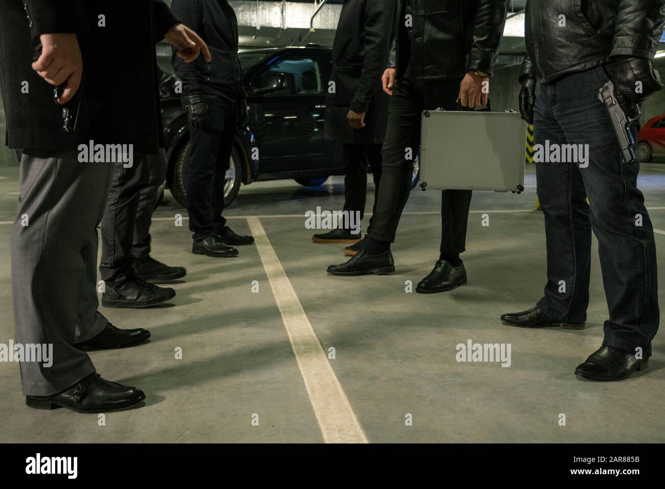Due file di uomini in nero con pistole e valigia in piedi sul parcheggio Foto Stock