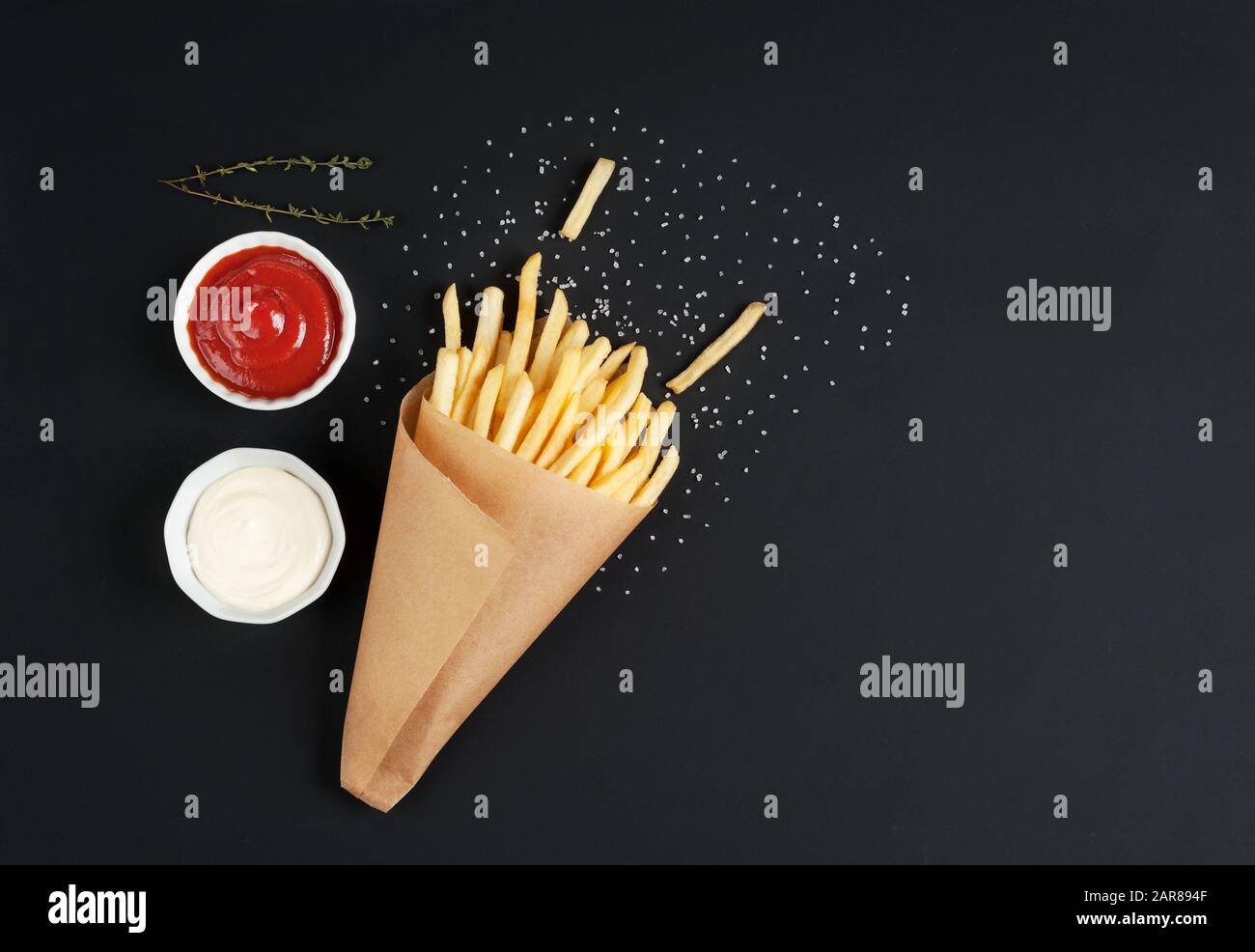 Gustose patatine fritte con salse, sale ed erbe su fondo scuro. Patatine nel cono di carta. Orizzontale con spazio per il testo. Foto Stock