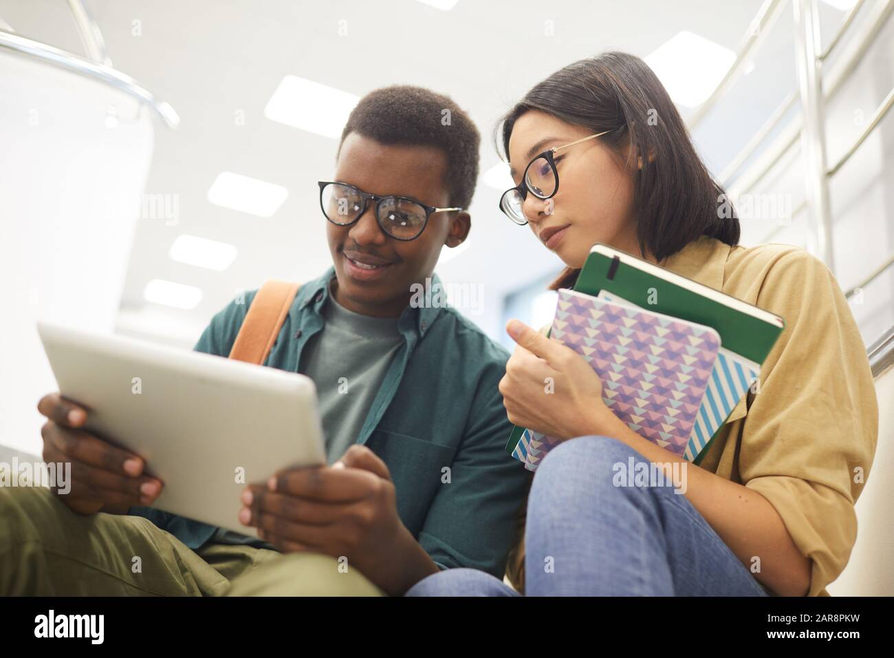 Ritratto di due studenti internazionali che leggono insieme libri mentre lavorano su progetto nella moderna biblioteca universitaria Foto Stock