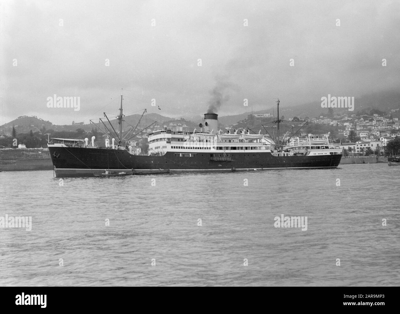 Vista Laterale di Madeira di una nave da passeggeri portoghese, con camino fumatore, nel porto di Funchal, Madeira, con la città sullo sfondo. Data: 1934 luogo: Funchal, Madeira, Portogallo Parole Chiave: Porti, navi, camini, cityscapes Nome dell'istituto: Colombia, KNSM Foto Stock