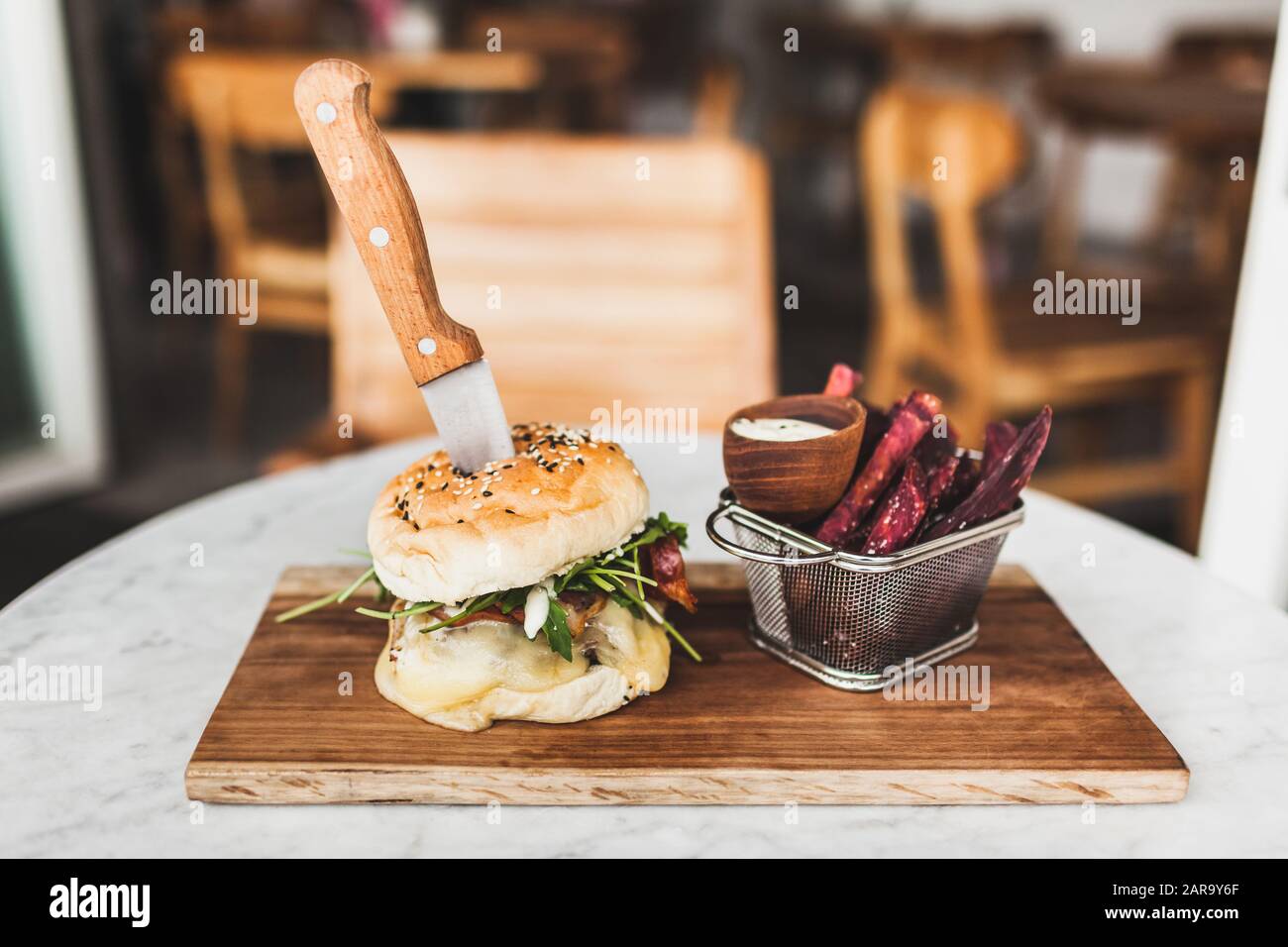 Freschi e saporiti burger con coltello all'interno con la salsa e fritto viola la patata dolce sul lato. Su bianco tavola rotonda sulla tavola di legno Foto Stock