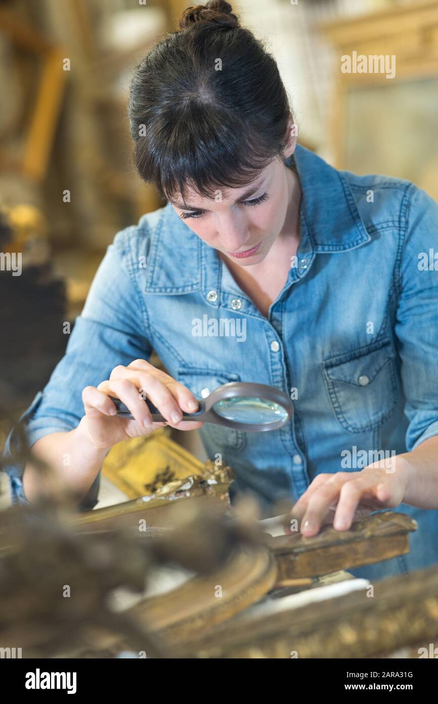 donna che usa una lente di ingrandimento per ispezionare un abbellimento della cornice Foto Stock