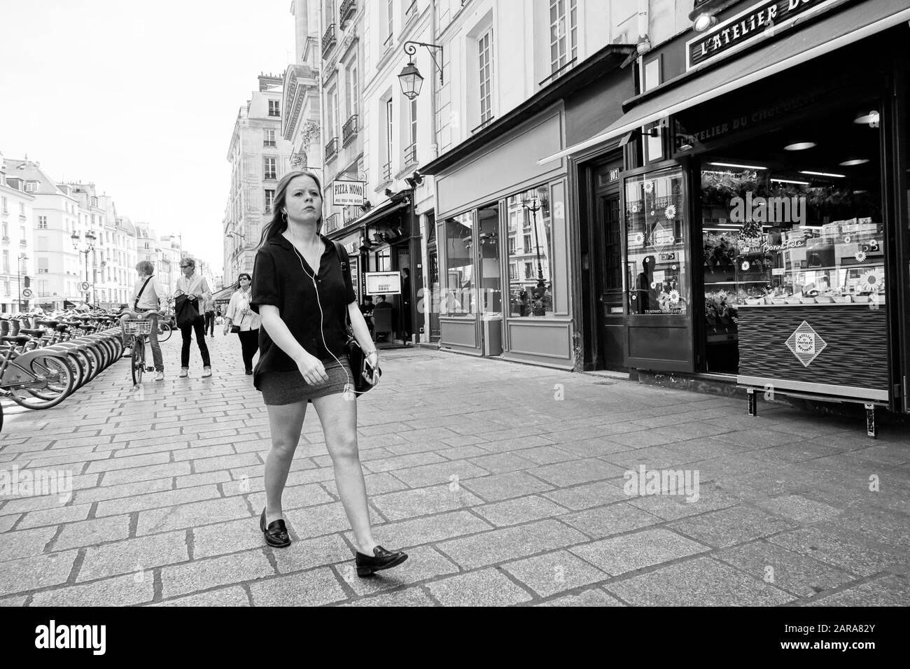 Ragazza che indossa gli auricolari a piedi sul marciapiede, Rue Saint Antoine, Parigi, Francia, Europa Foto Stock