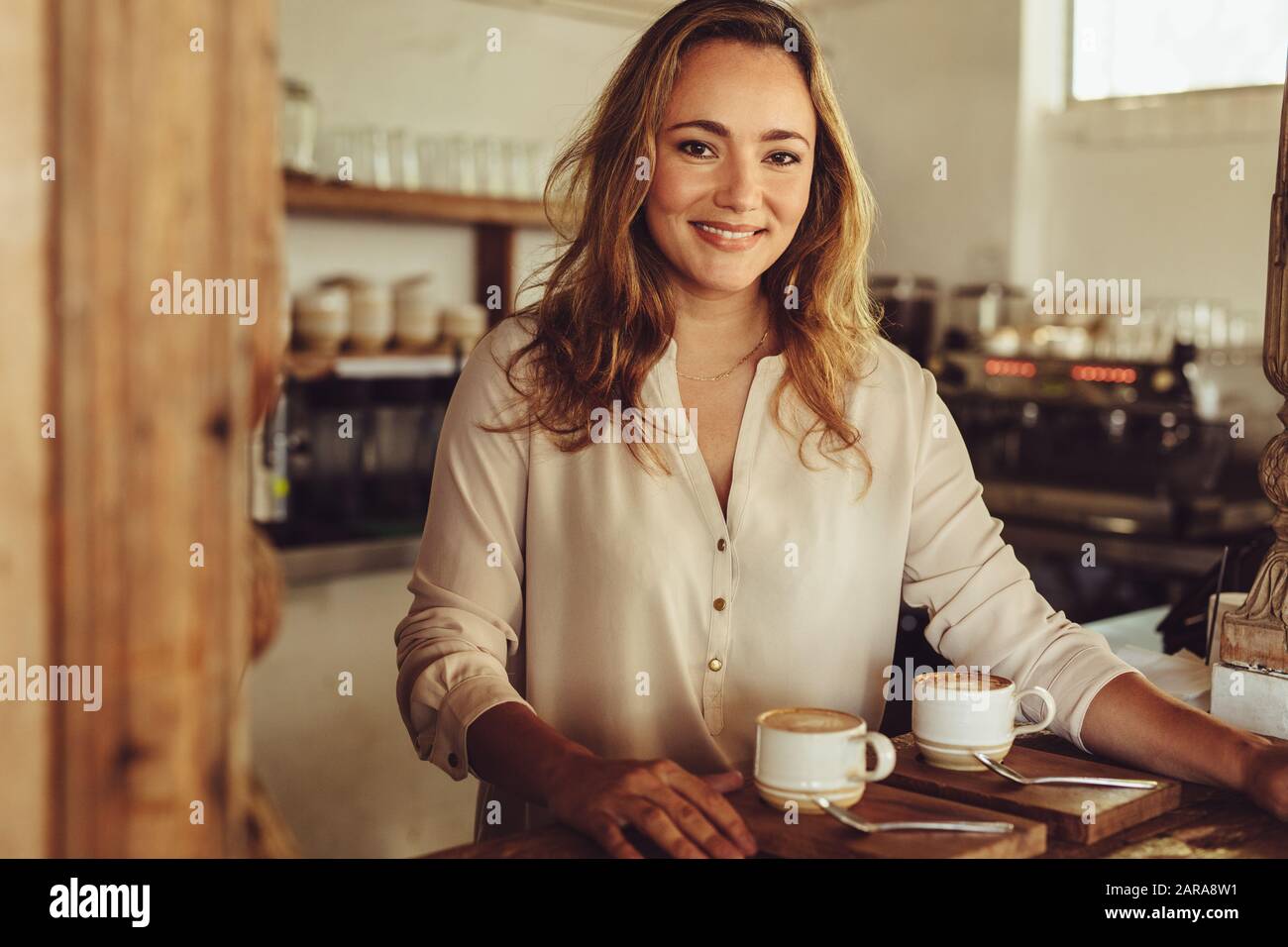 Ritratto di una giovane donna che lavora dietro il bancone di una caffetteria. Barista femminile sorridente che serve il caffè. Foto Stock