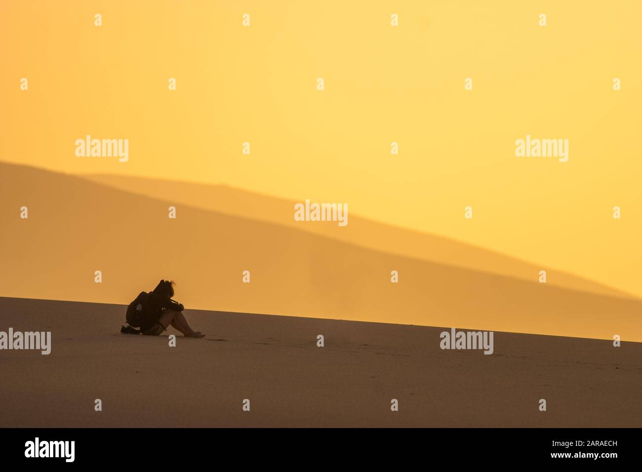 silhouette di un turista seduto su una duna del deserto Foto Stock