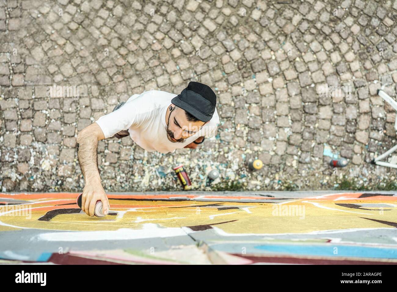 Giovane scrittore graffiti pittura con colore spray la sua foto sul muro - Top con artisti contemporanei al lavoro - stile di vita urbano, strada illegale ar Foto Stock