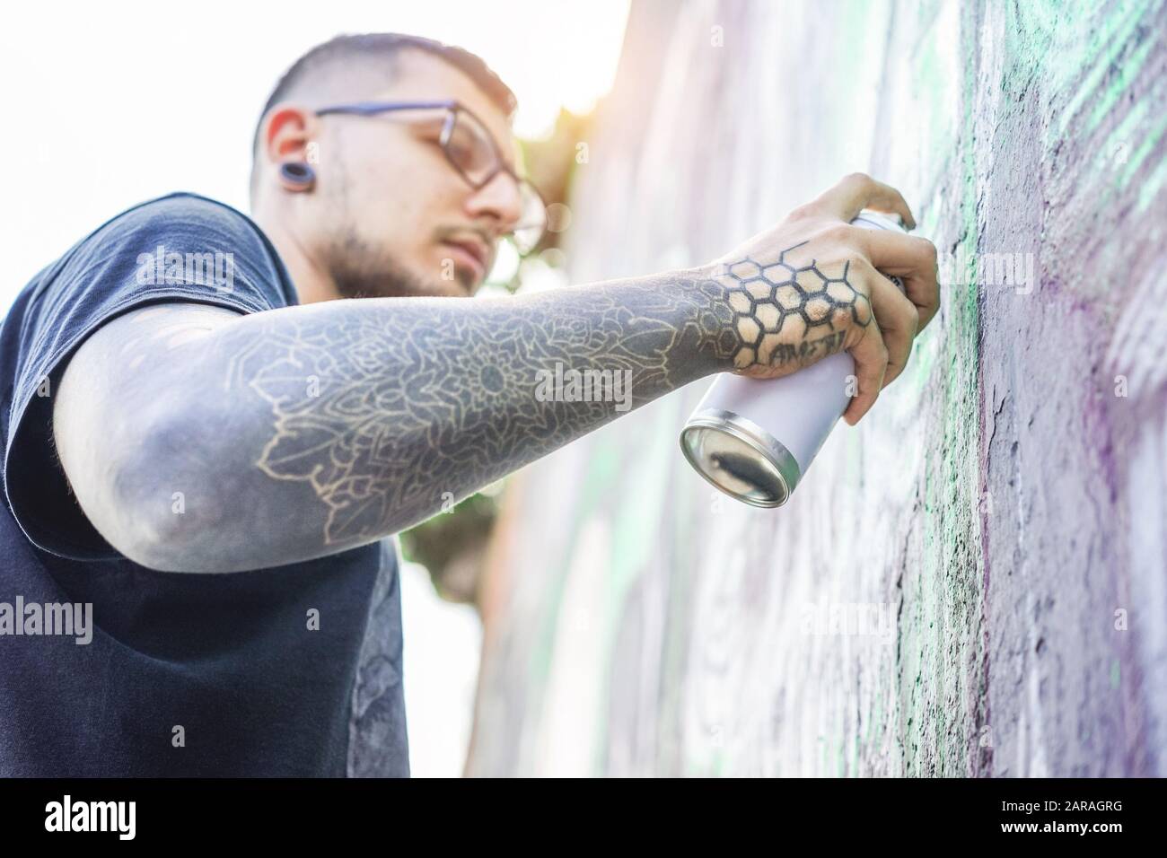 Graffiti tatuati artista pittura con aerosol a colori sul muro - spray contemporaneo scrivere al lavoro - stile di vita urbano, Street art concept - Focus on hi Foto Stock