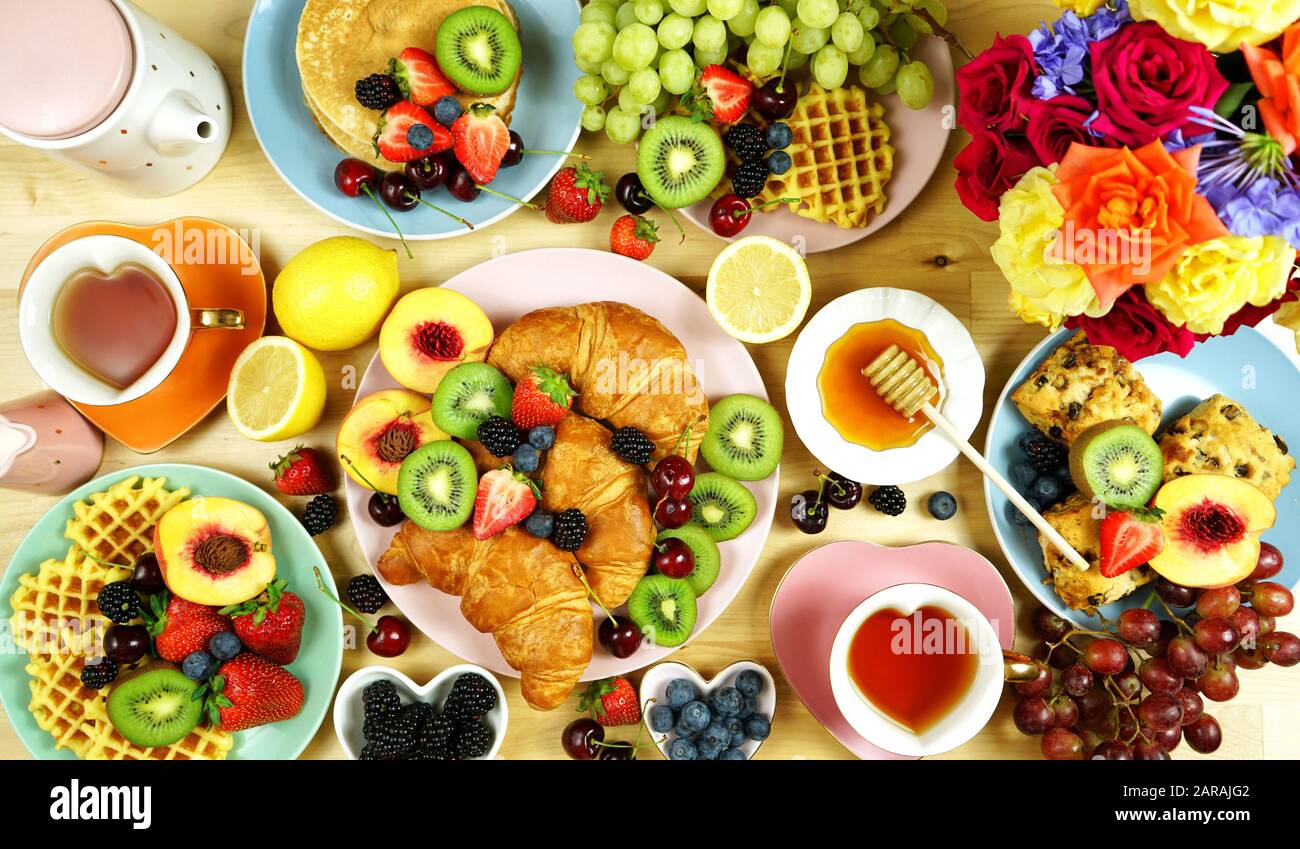 Colazione creativa a buffet con croissant, pancake, waffle, frutta e rose. Vista dall'alto. Foto Stock