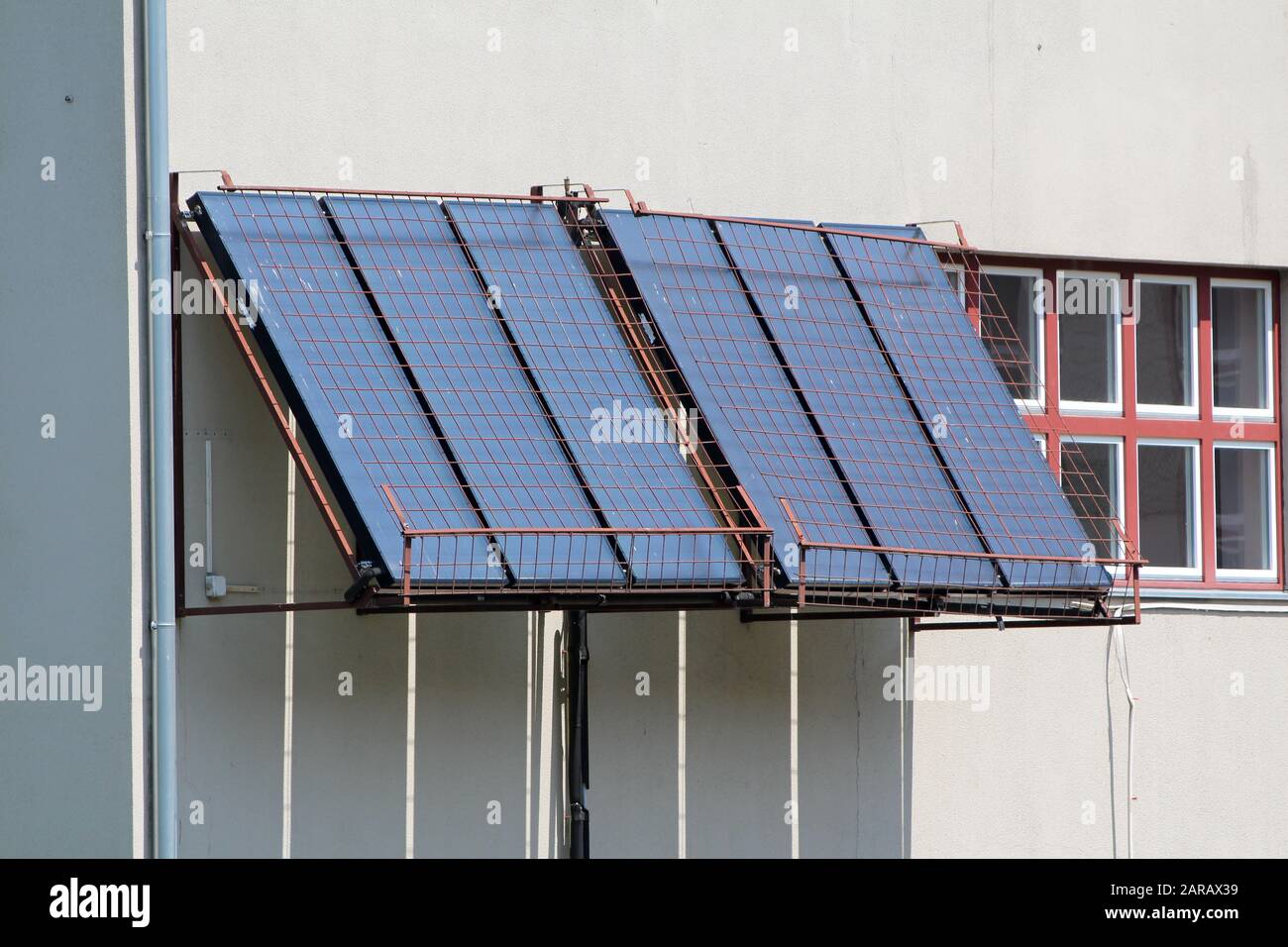 Sei grandi pannelli solari per il riscaldamento dell'acqua coperti da rete metallica per la protezione montata sulla parete laterale locale della scuola superiore accanto alla fila di piccole finestre Foto Stock