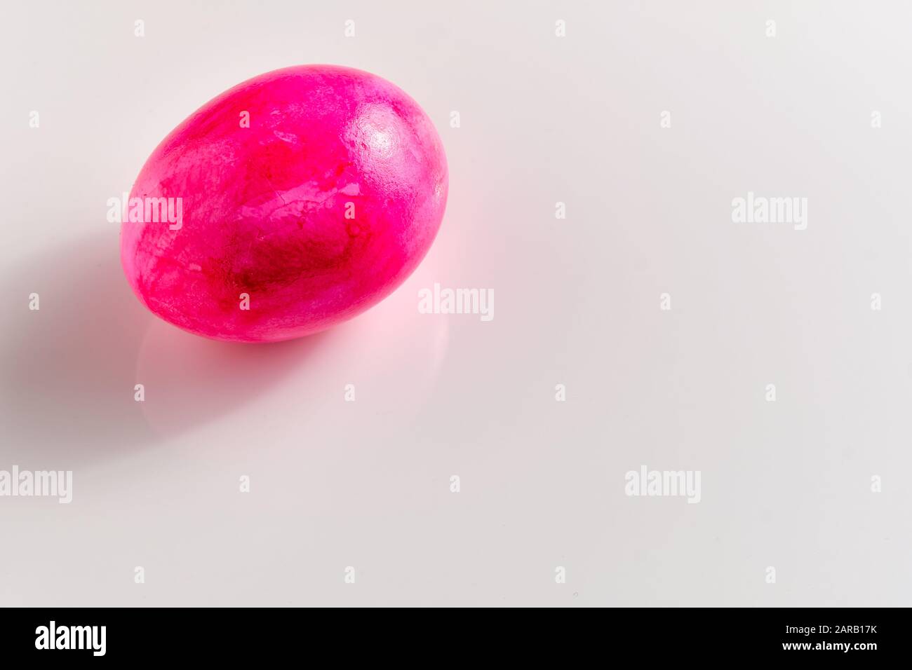 Uovo di pasqua rosa brillante con alcune prime piccole crepe sottili nel guscio d'uovo sdraiato su terreno bianco con spazio copia Foto Stock