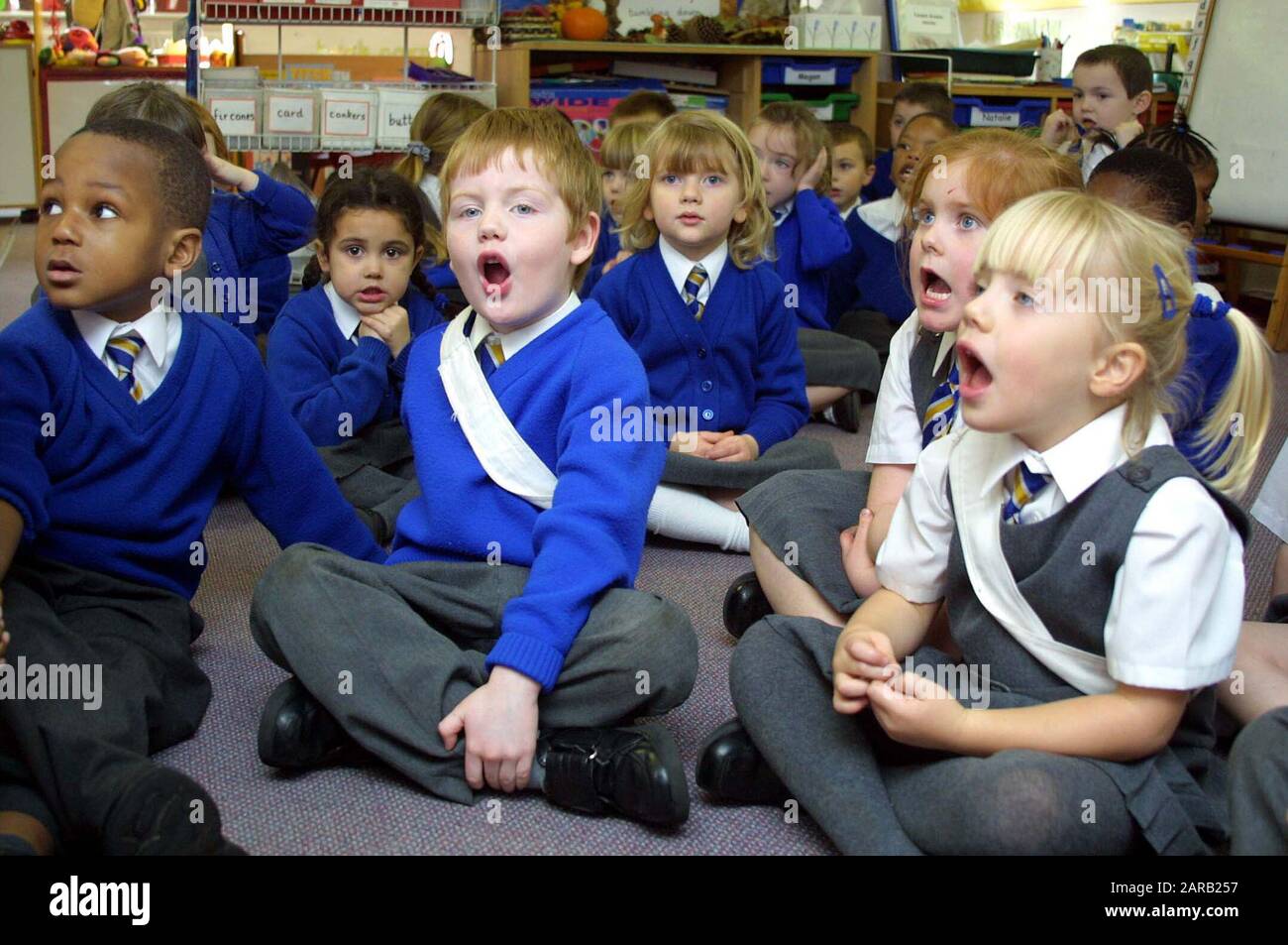 Bambini studenteschi unibformed che cantano seduti su un piano della classe in un'aula di villaggio Foto Stock