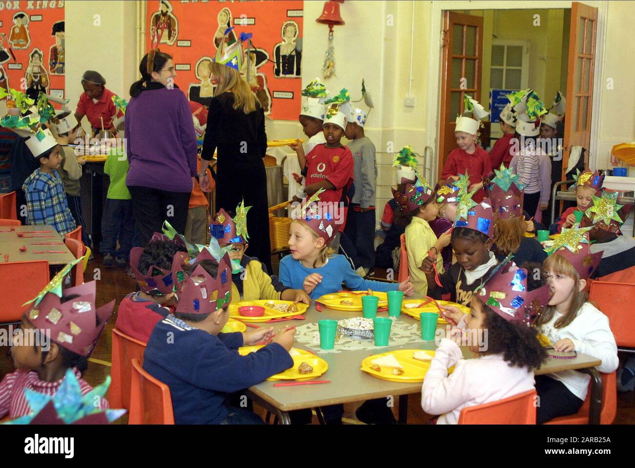 Scuola del villaggio Natale celebrazione in aula con i bambini della scuola primaria che hanno un pasto che indossa cappelli decorati Foto Stock
