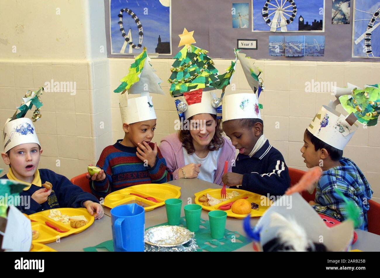 Scuola del villaggio Natale celebrazione in aula con i bambini della scuola primaria e insegnante che ha un pasto che indossa cappelli decorati Foto Stock