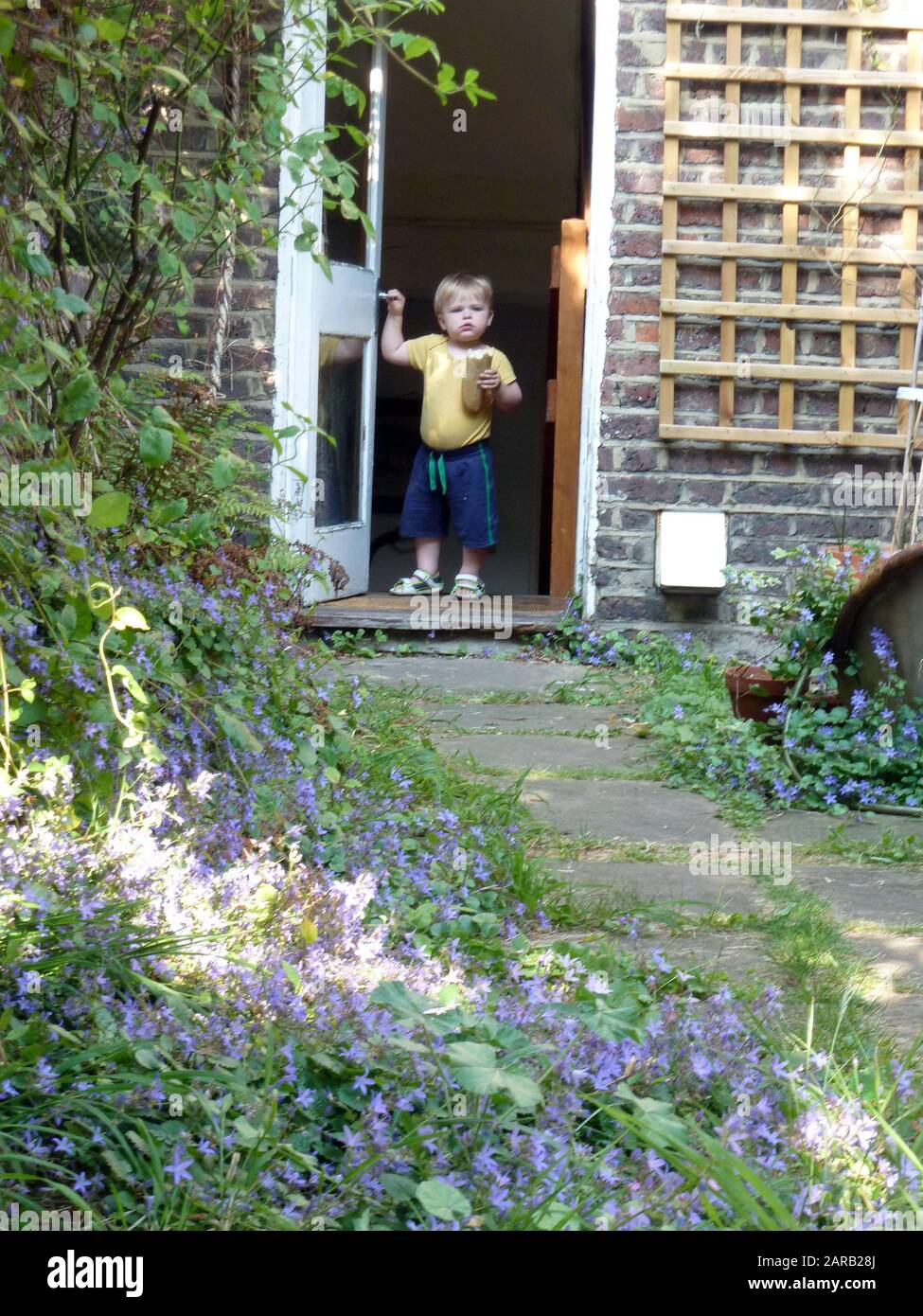 Un toddler ad una porta aperta al giardino che tiene una pagnotta di pane Foto Stock