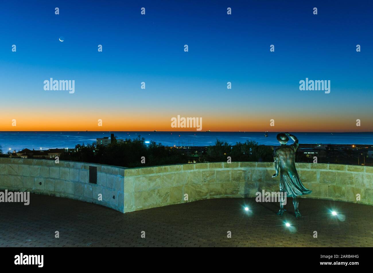 La sera, la statua in bronzo di una donna, con il suo cappello nella brezza marina, si affaccia sul porto di Geraldton presso il monumento commemorativo HMAS Sydney 11. Foto Stock