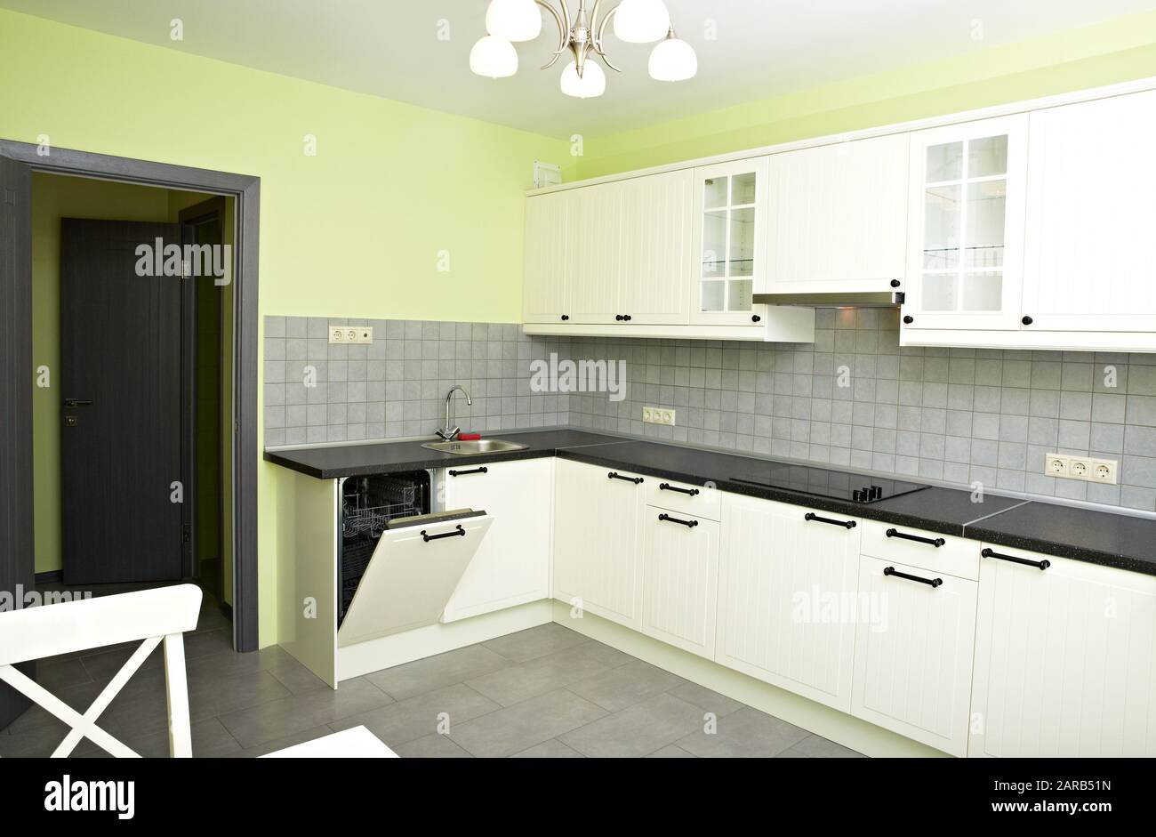 Nuova piccola cucina bianca in una stanza con pareti verdi. Piano di appoggio nero, lavastoviglie, vetrine in vetro, lavello. Foto Stock