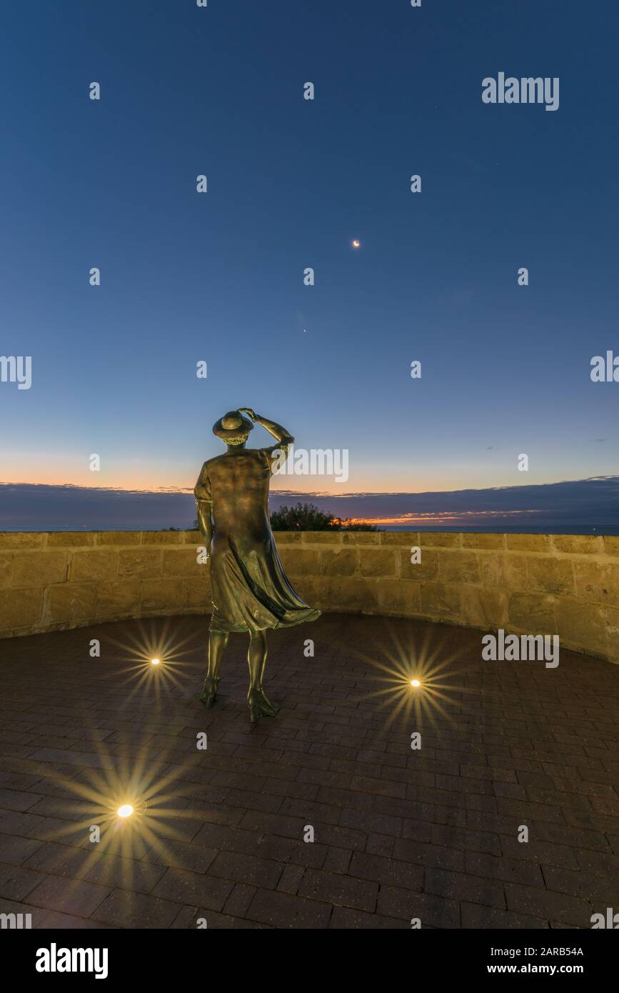 La sera, la statua in bronzo di una donna, con il suo cappello nella brezza marina, si affaccia sul porto di Geraldton presso il monumento commemorativo HMAS Sydney 11. Foto Stock