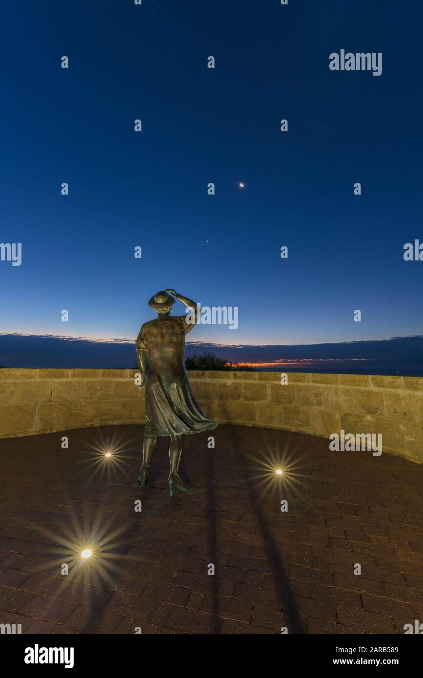 La sera, la statua in bronzo di una donna, con il suo cappello nella brezza marina, si affaccia sul porto di Geraldton presso il monumento commemorativo HMAS Sydney 11. Foto Stock