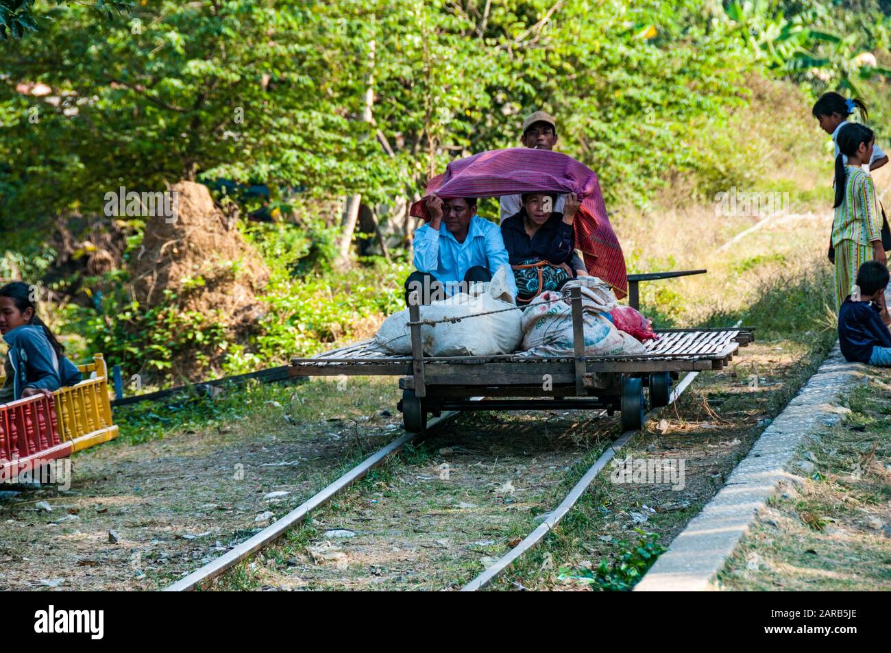 Due cambogiani sorridente e riparo sotto un foglio con merci su un treno di bambù di O Sra Lav station Foto Stock