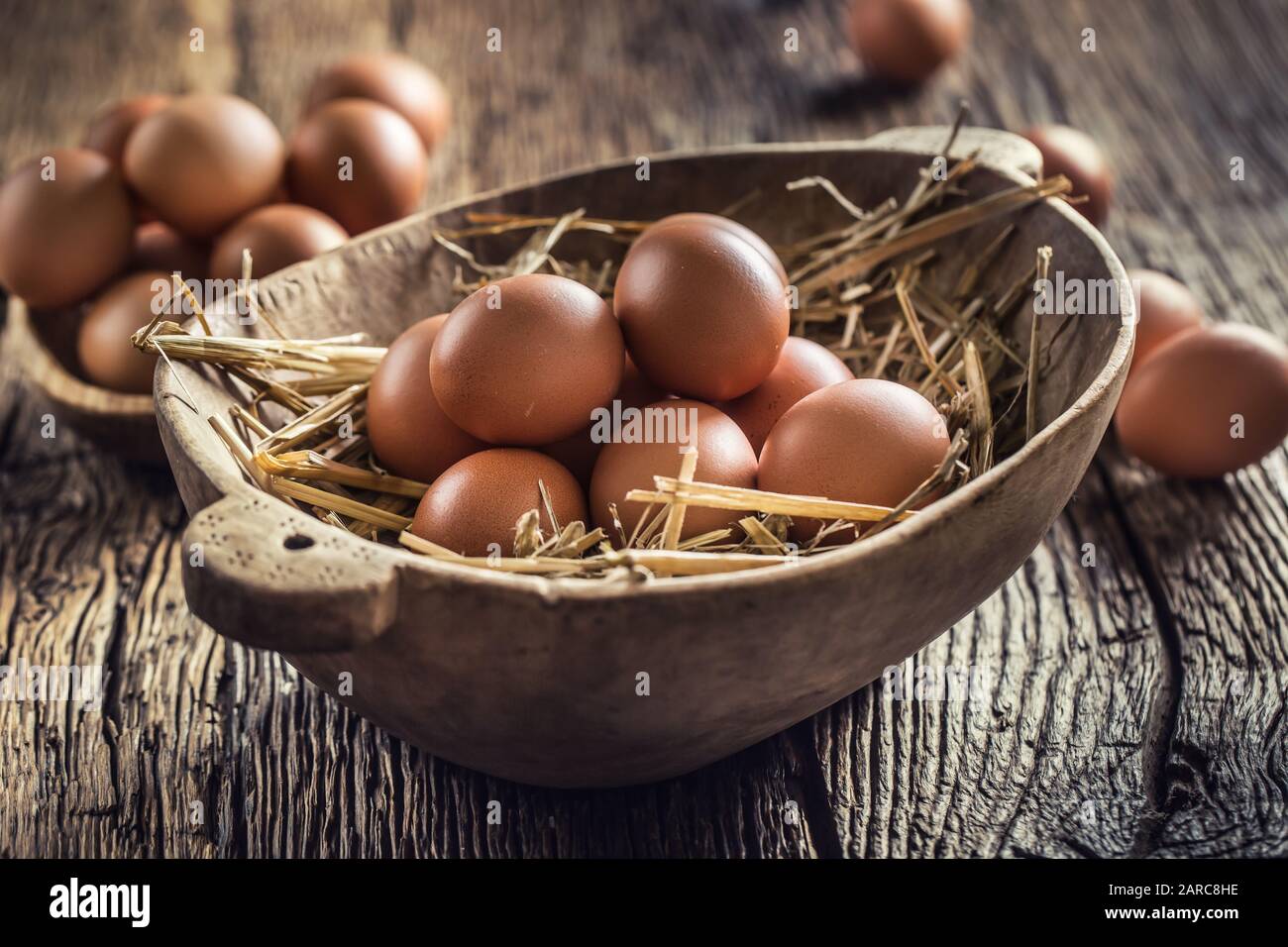 Uova fresche crude in paglia e ciotola di legno su tavola rustica di legno Foto Stock