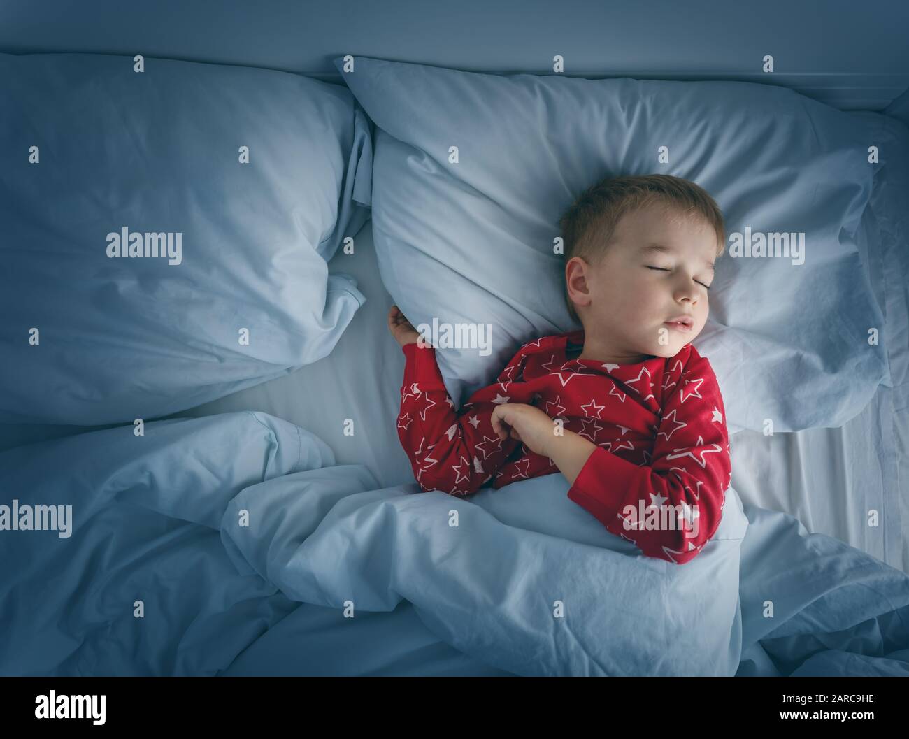 Ragazzo assonnato sdraiato a letto con letti blu. Bambino stanco in camera da letto Foto Stock