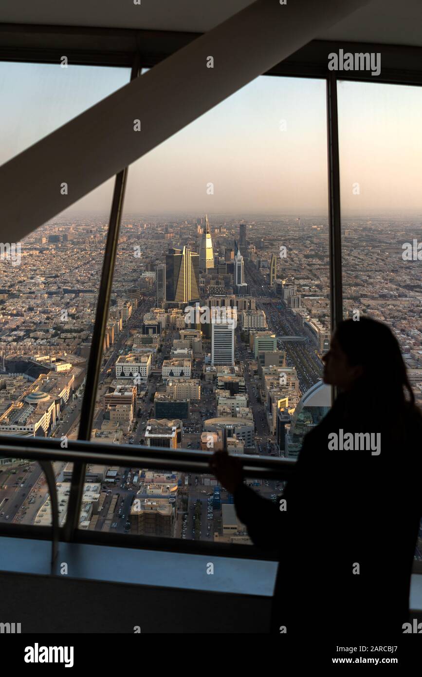 Viaggiatore straniero femminile in abaya nero che si affaccia sullo skyline di Riyadh in Arabia Saudita da un grattacielo nel centro della città durante il tramonto Foto Stock