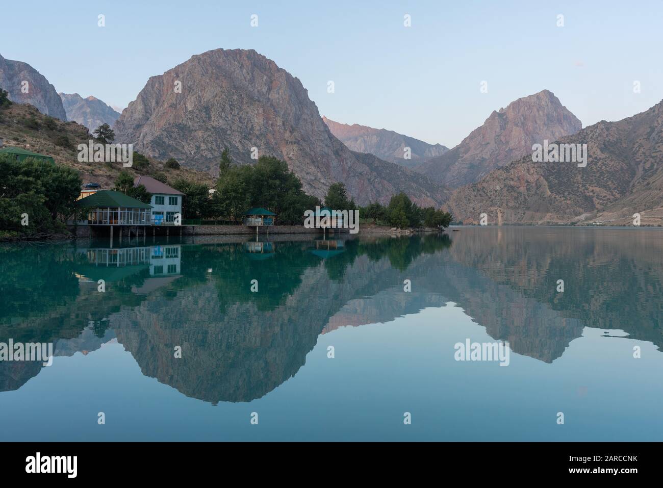 Edifici turistici sul bordo delle acque turchesi del lago Iskanderkul in Tagikistan con le montagne sullo sfondo Foto Stock