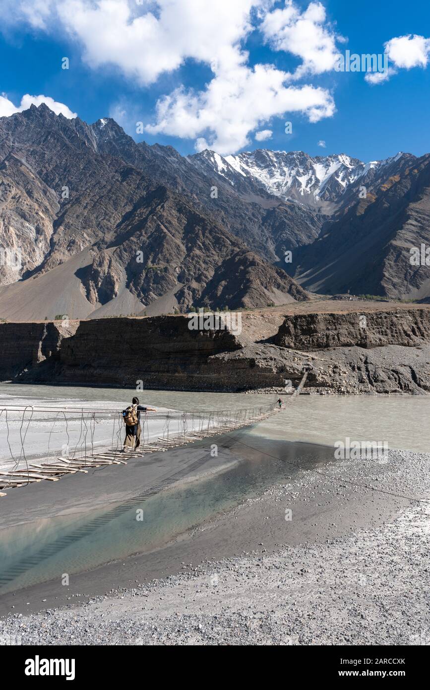 Viaggiatore femminile con zaino a piedi attraverso un pericoloso ponte sospeso sulle montagne di Gilgit Baltistan, Pakistan Foto Stock