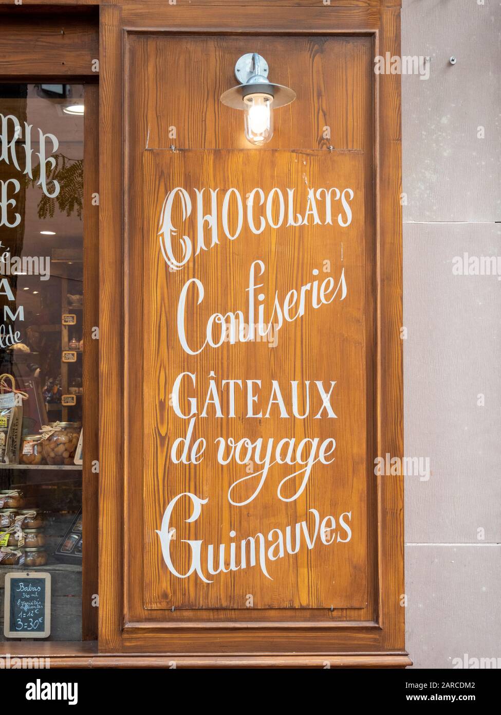 Una tavola di legno o una finestra di serranda fuori di un negozio di cioccolato francese con scrittura di cioccolatini pubblicitari, confiseries, gateaux de voyage e altri dolci Foto Stock