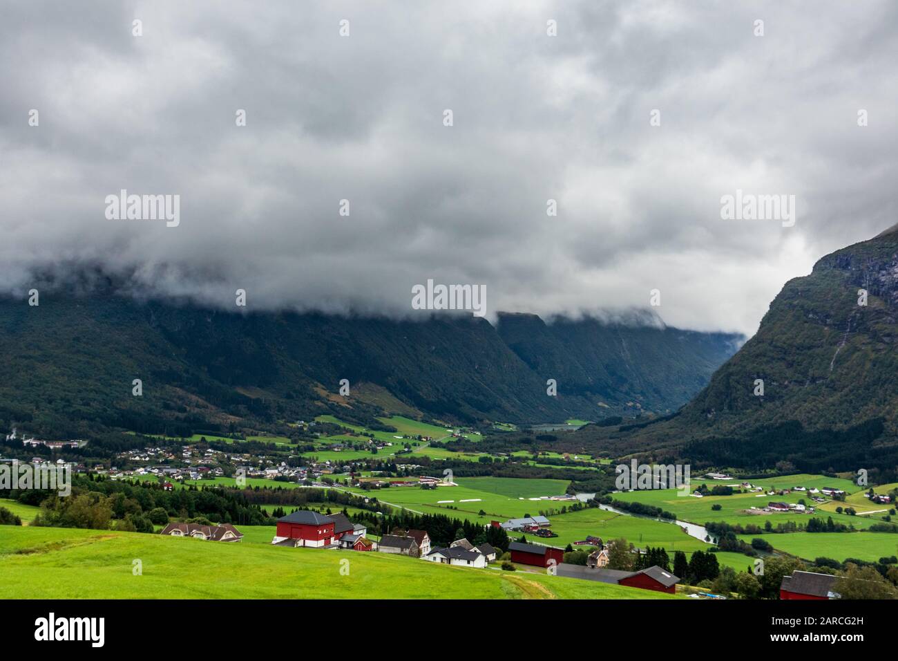 Prati verdi nella campagna norvegese vicino alle montagne. Giorno estivo nebbia nuvoloso, paesaggio rurale norvegese panoramico. Foto Stock