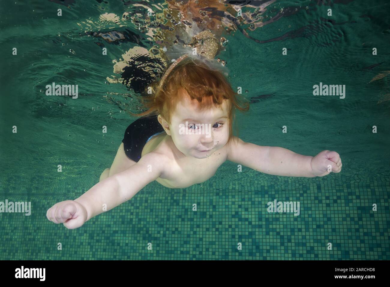 La bambina redhead impara a nuotare sott'acqua. Baby nuoto sott'acqua in piscina su sfondo blu acqua. Sano stile di vita familiare e bambini Foto Stock