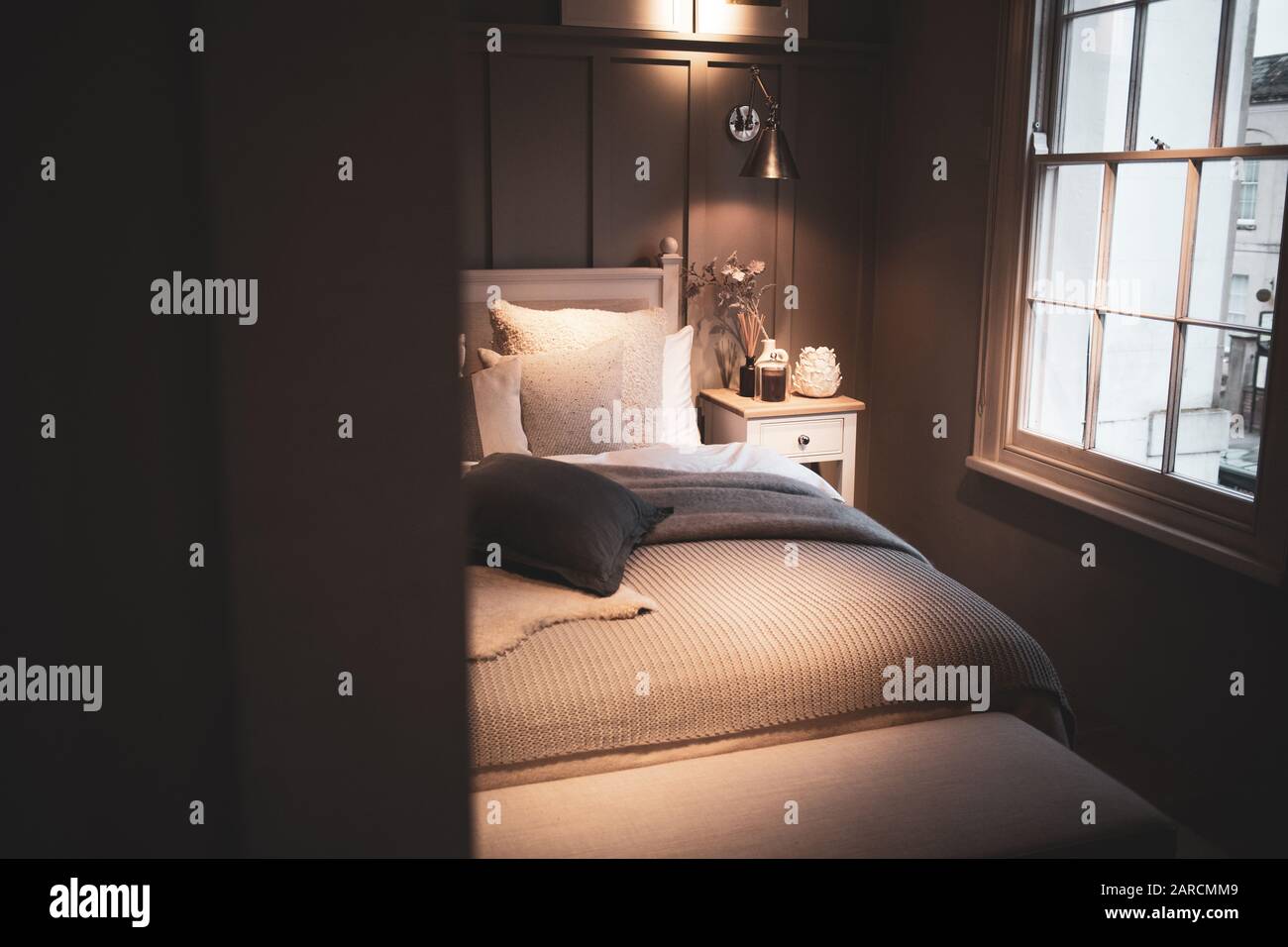 Bella camera da letto in stile classico neutro con pannelli in legno e una finestra di frassino che getta luce soffusa sul letto. Foto Stock