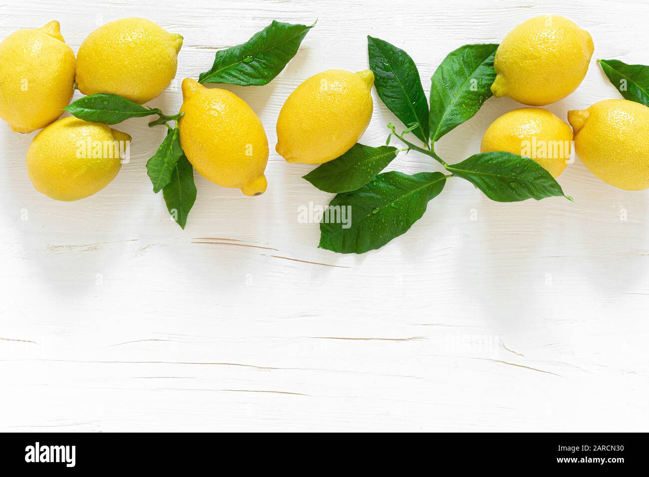 Limoni freschi con foglie su sfondo di legno bianco, ingrediente limonata estiva, concetto di vitamina c, vista dall'alto Foto Stock