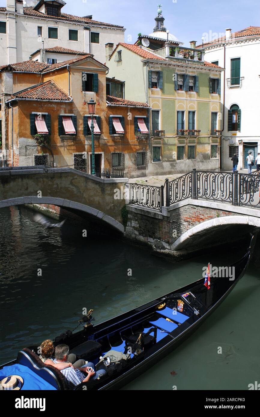 Un giro in gondola in coppia mentre si manovra sotto un ponte su un canale a Venezia, Italia Foto Stock