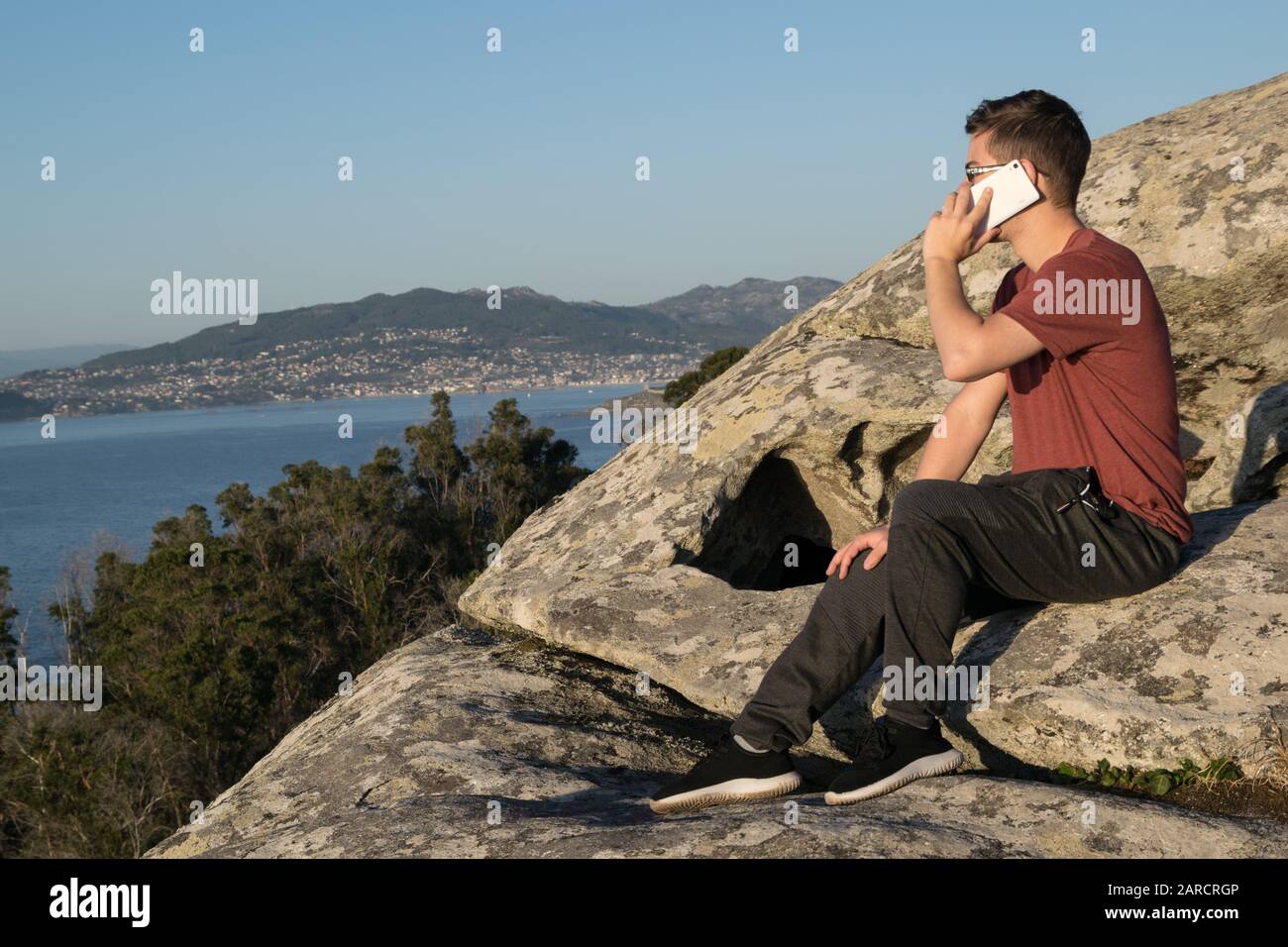 Uomo seduto su una roccia che parla sul telefono cellulare Foto Stock